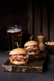 Leckere Hamburger mit Pulled Pork und Krautsalat in knusprigen Brötchen, serviert auf einem rustikalen Holzbrett - ADSF24183