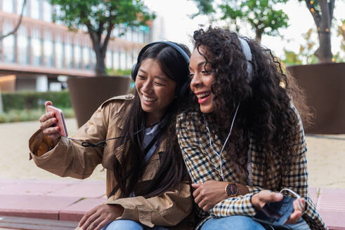 Asiatische Frau, die mit ihrem Smartphone telefoniert, und eine fokussierte schwarze Frau, die Musik hört und auf ihrem Handy im Internet surft - ADSF24206