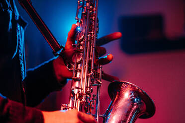 Gesichtsloser Berufsmusiker spielt Saxophon mit den Fingern auf den Tasten bei einem Live-Konzert in Neonlicht - ADSF24222