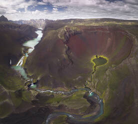 Erstaunlicher Blick auf die kurvenreiche blaue Flussschleife, die durch das raue, hügelige Gelände mit üppiger Vegetation in Island fließt - ADSF24224