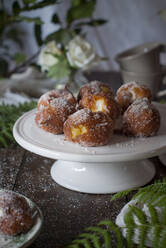 Hausgemachte Puddingcremekrapfen mit Zucker bestreut auf rustikalem Holztisch mit Tischtuch und Blättern als Dekoration - ADSF24233