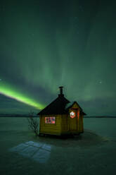 Schöne Aurora Borealis (Nordlicht) über einer Holzhütte am See Tornetrask in Nordschweden, Skandinavien, Europa - RHPLF19775