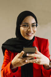Lächelnde Frau mit Hidschab, die in einem Café ein Mobiltelefon hält - XLGF01830