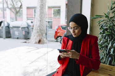 Young woman wearing hijab using mobile phone at cafe - XLGF01833