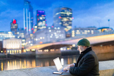 Mann arbeitet am Laptop an der Themse, London, UK - CUF57943