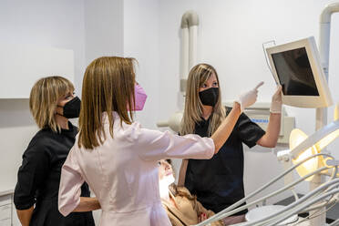 Female dentist with assistants analyzing x-ray in medical clinic during COVID-19 - DLTSF01892