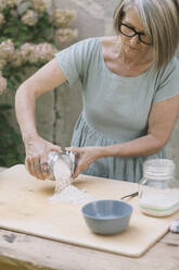 Ältere Frau, die Mehl auf ein Brett im Hinterhof legt - ALBF01590