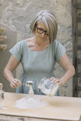 Ältere Frau mit Löffel bereitet Teig im Hinterhof vor - ALBF01592