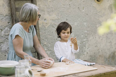 Reife Frau betrachtet Enkel, der mit Knete im Hinterhof spielt - ALBF01601