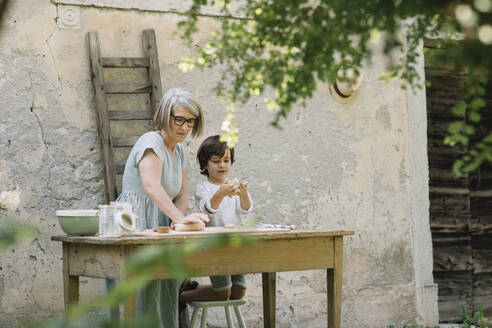 Großmutter knetet Teig auf dem Tisch des Enkels im Hinterhof - ALBF01602