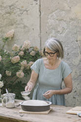 Mature woman sprinkling powdered sugar through sieve while preparing bread at backyard - ALBF01612