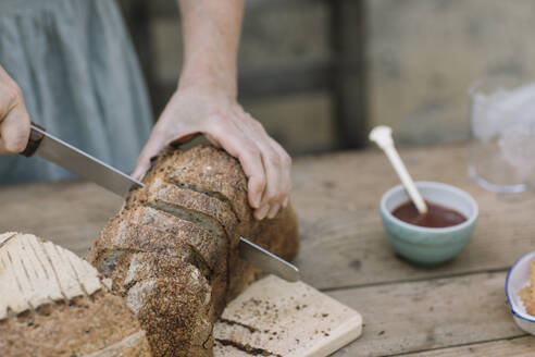 Mature woman cutting bread with knife on table - ALBF01627