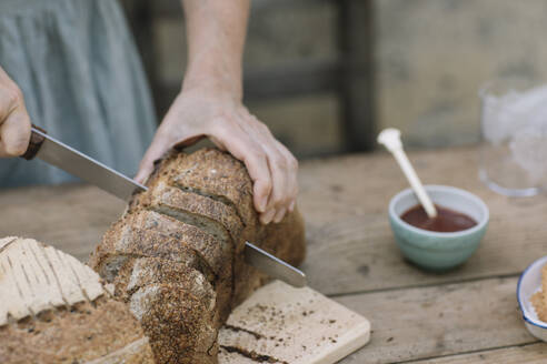 Reife Frau schneidet Brot mit Messer auf Tisch - ALBF01627