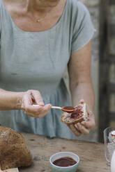Reife Frau trägt Soße auf Brot im Hinterhof auf - ALBF01628