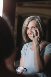 Lächelnde Frau schaut in den Spiegel, während sie sich zu Hause eincremt - ALBF01633