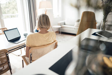 Kurzhaarige Geschäftsfrau mit Blick auf den Laptop im Wohnzimmer - JOSEF04521