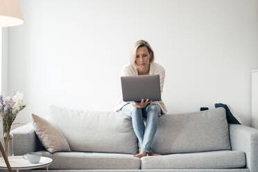 Mid adult woman using laptop on sofa at home - JOSEF04545