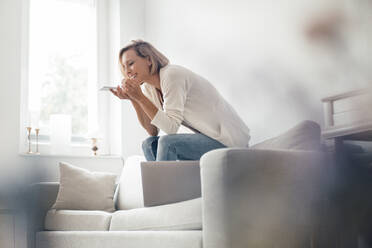 Lächelnde Frau, die auf dem Sofa zu Hause telefoniert - JOSEF04548