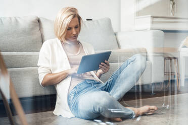 Blond hair woman with digital tablet sitting on floor at home - JOSEF04550
