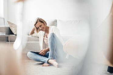 Smiling woman using digital tablet on floor at home - JOSEF04551