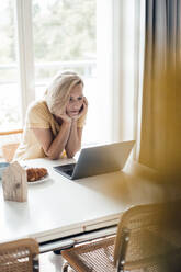 Female professional with hand on chin using laptop at home - JOSEF04557