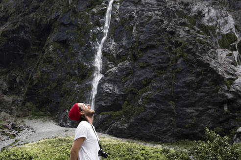 New Zealand, South Island, Fiordland National Park, Young man pretending to drink waterfall - WVF01857