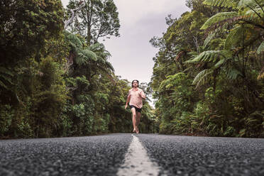 Neuseeland, Nordinsel, Northland, Junger Mann läuft auf Straße durch Waipoua Forest - WVF01873