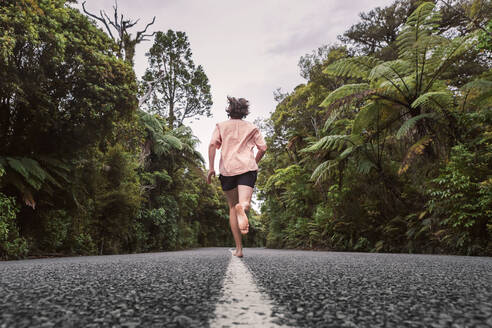 Neuseeland, Nordinsel, Northland, Junger Mann läuft auf Straße durch Waipoua Forest - WVF01874
