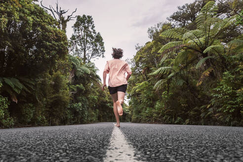 New Zealand, North Island, Northland, Young man running on road through Waipoua Forest - WVF01874