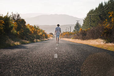 New Zealand, North Island, Rotorua, Rear view of young man walking on road in Bay of Plenty - WVF01876