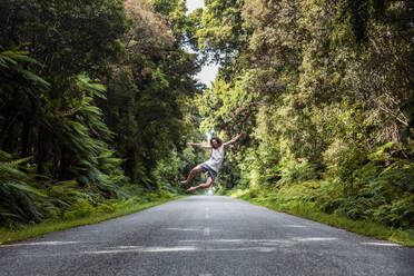 Man jumping in middle of forest highway - WVF01927