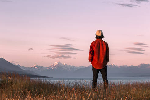 Neuseeland, Canterbury, Rückansicht eines jungen Mannes mit Blick auf den Lake Pukaki bei Sonnenuntergang - WVF01931