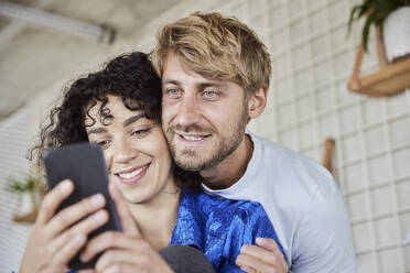 Junge Frau mit Freund, der ein Mobiltelefon benutzt - FMKF07133