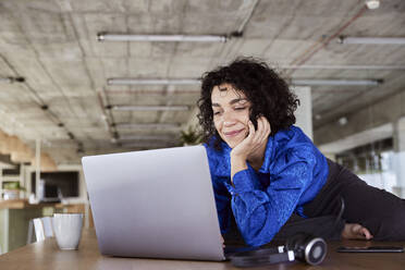 Lächelnde Frau mit Laptop auf dem Tisch im Loft - FMKF07135