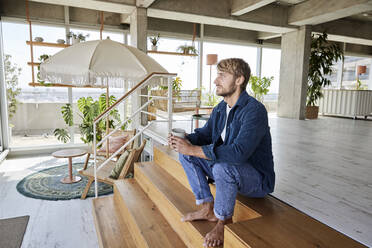 Handsome man sitting on steps at loft - FMKF07138