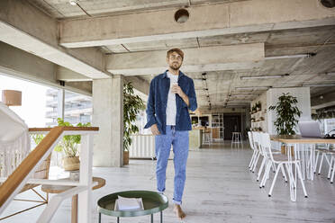 Man holding mug while walking at loft - FMKF07139