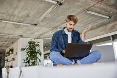 Man gesturing while using laptop at loft - FMKF07144