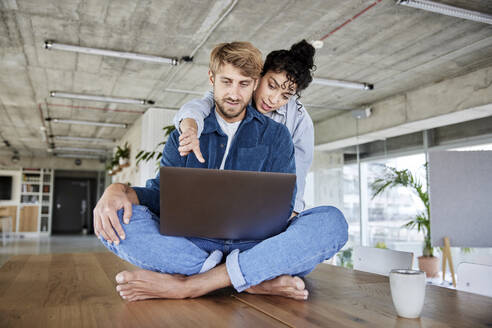 Frau, die auf einen Laptop zeigt, während sie mit ihrem Freund auf einem Tisch im Loft sitzt - FMKF07147