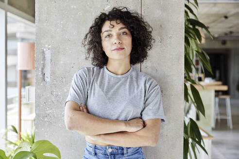 Confident woman with arms crossed standing in front of column at loft - FMKF07160