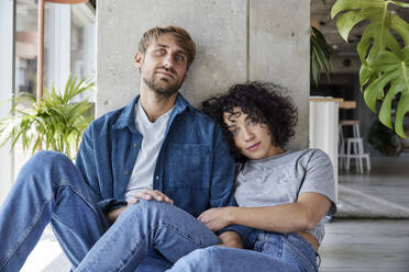 Müdes Paar, das sich auf eine Säule stützt, während es in seiner Wohnung auf dem Boden sitzt - FMKF07180
