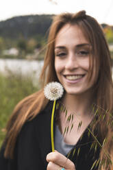 Schöne Frau lächelnd mit Blick auf Pusteblume - JAQF00618