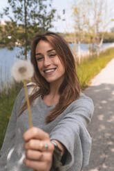 Smiling woman showing blowball in nature - JAQF00620