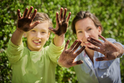 Mutter mit Sohn zeigt Schlamm Hände im Garten während sonnigen Tag - DIKF00582