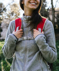 Anonyme glückliche optimistische junge Wanderin in Sportkleidung mit Rucksack genießt Reise in grünen Wald in sonnigen Tag - ADSF24259