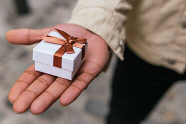 Anonyme männliche Hand, die ein kleines Geschenkpaket mit Schleife in der Stadt hält - ADSF24269