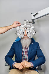 Crop unrecognizable optician using phoropter for eyesight testing of senior male patient in clinic - ADSF24286