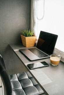 Moderner Laptop und Smartphone auf dem Tresen mit einer Tasse Morgenkaffee in der von Sonnenlicht beleuchteten Küche - ADSF24316