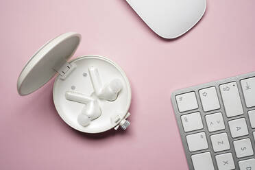 Draufsicht Komposition von weißen True Wireless Earbuds im Etui in der Nähe von Laptop-Tastatur und Maus auf rosa Schreibtisch platziert - ADSF24348