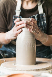 Cropped unrecognizable female artisan creating clay tableware on pottery wheel while working in art studio - ADSF24370