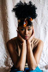 Ruhige schwarze Frau mit modischem Stirnband und Afrofrisur, die sich auf die Hände stützt und in die Kamera schaut, auf beigem Hintergrund - ADSF24394